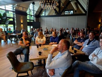 Landwinkeliers in de zaal kijken naar het zetten van de handtekening voor samenwerking met Postuma AGF en brancheorganisatie AVN